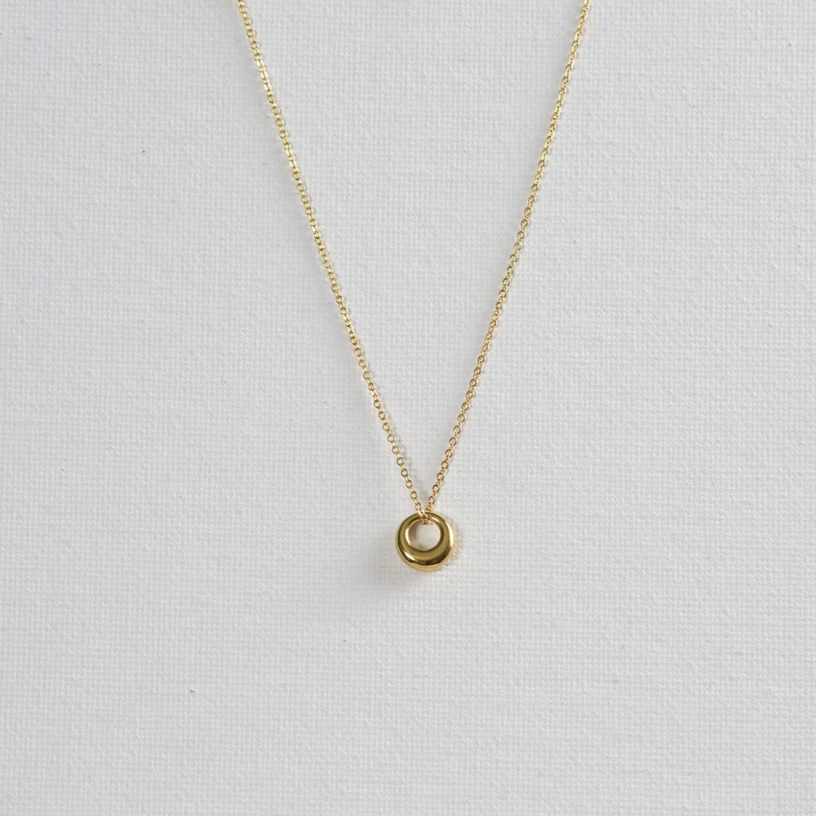 Gold Circle Pendant Necklace on a white background. The pendant features a unique shape, thinner on top and gradually thickening towards the bottom.