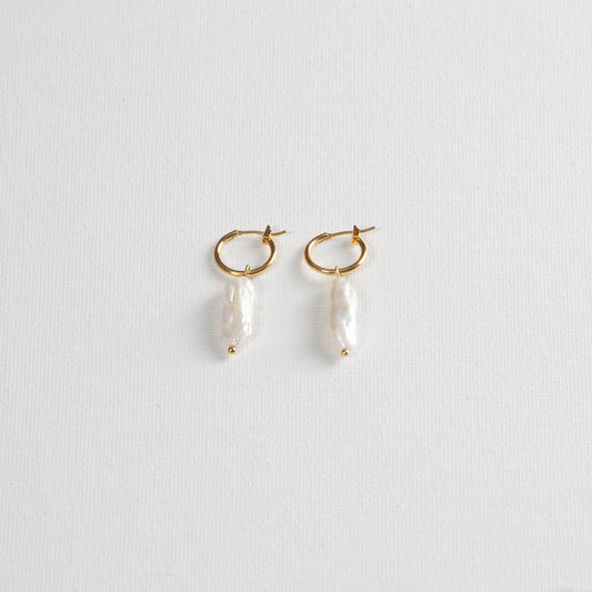 Delicate gold hoops with baroque pearl pendant on a white background.