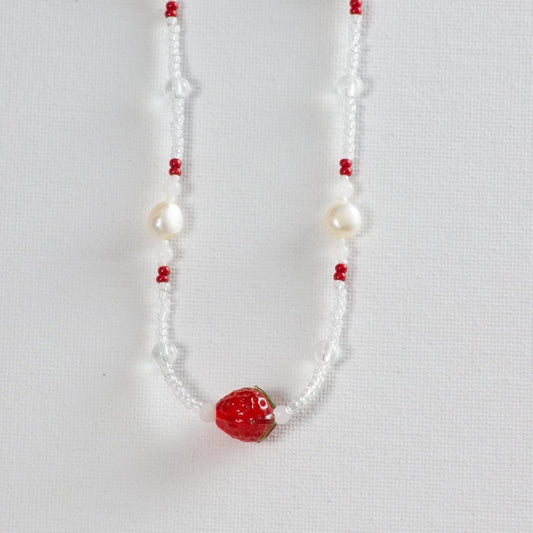 Beaded necklace with primarily small clear glass beads and accents of larger clear glass beads, pearl, red, milky white beads to add texture and pops of color. The necklace is photographed on a white background.