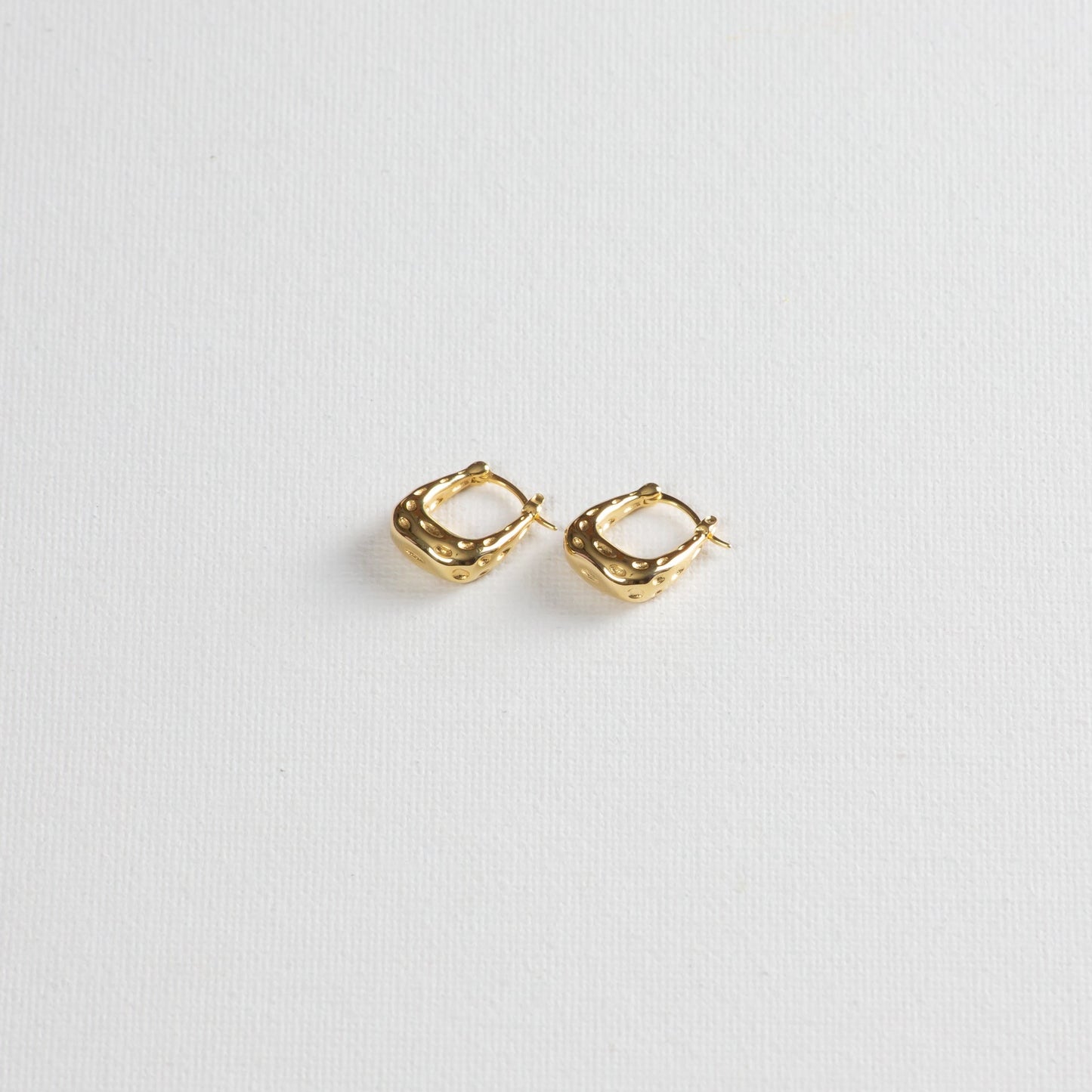 A rounded square-shaped hoop, hollow design with a dimpled texture on the outside, captured on a white background