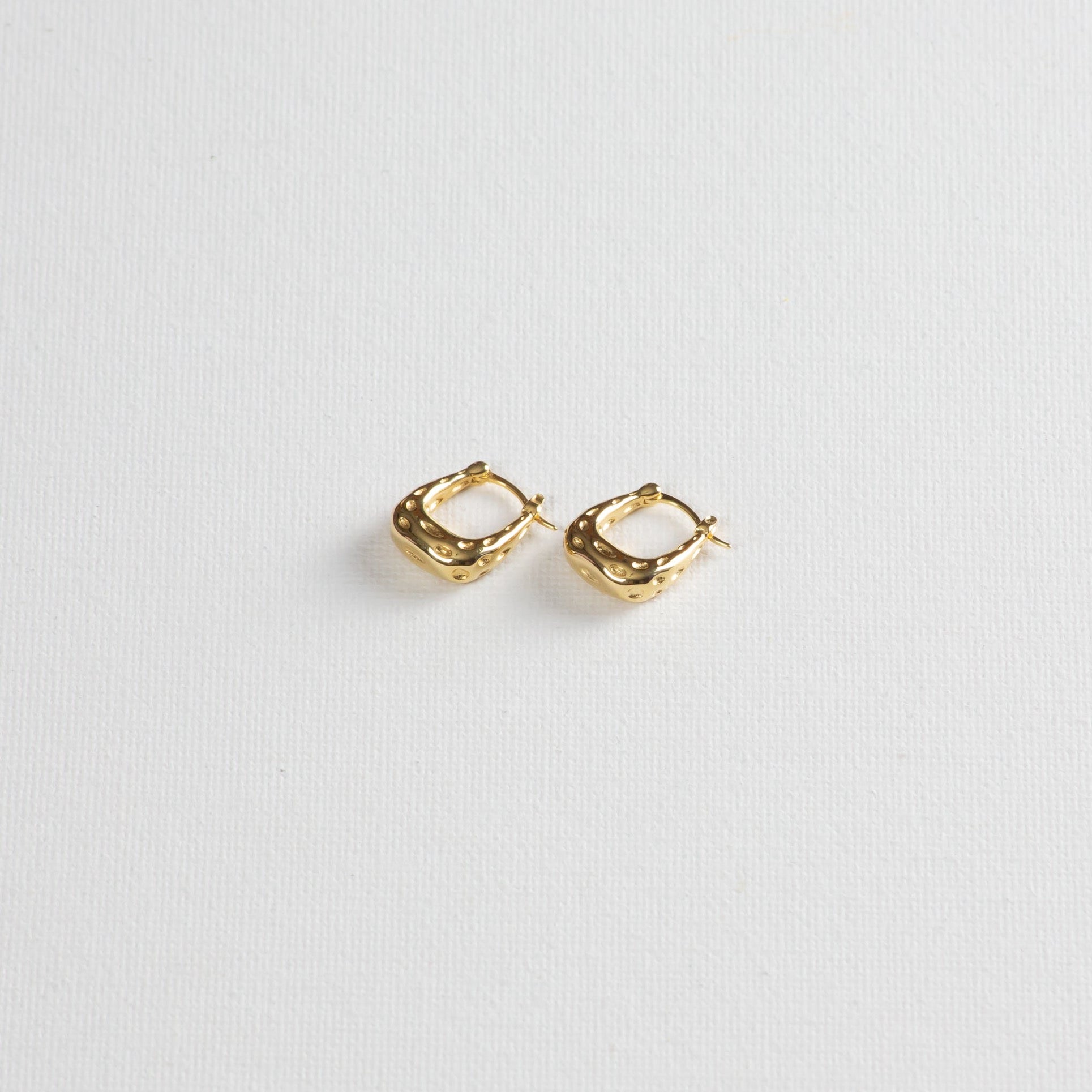 A rounded square-shaped hoop, hollow design with a dimpled texture on the outside, captured on a white background