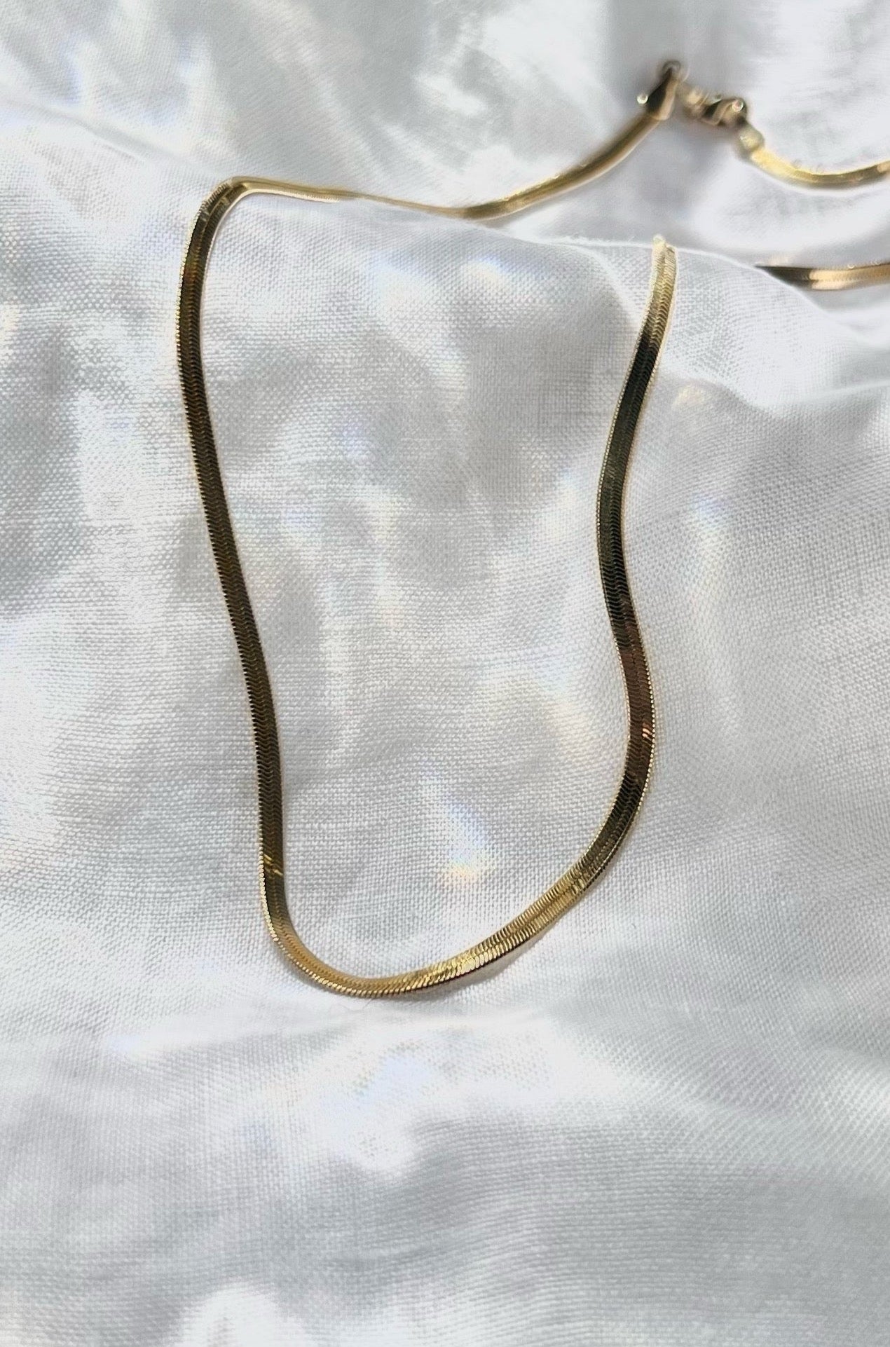 The gold chain necklace flows and shines like liquid gold on top of a white linen.