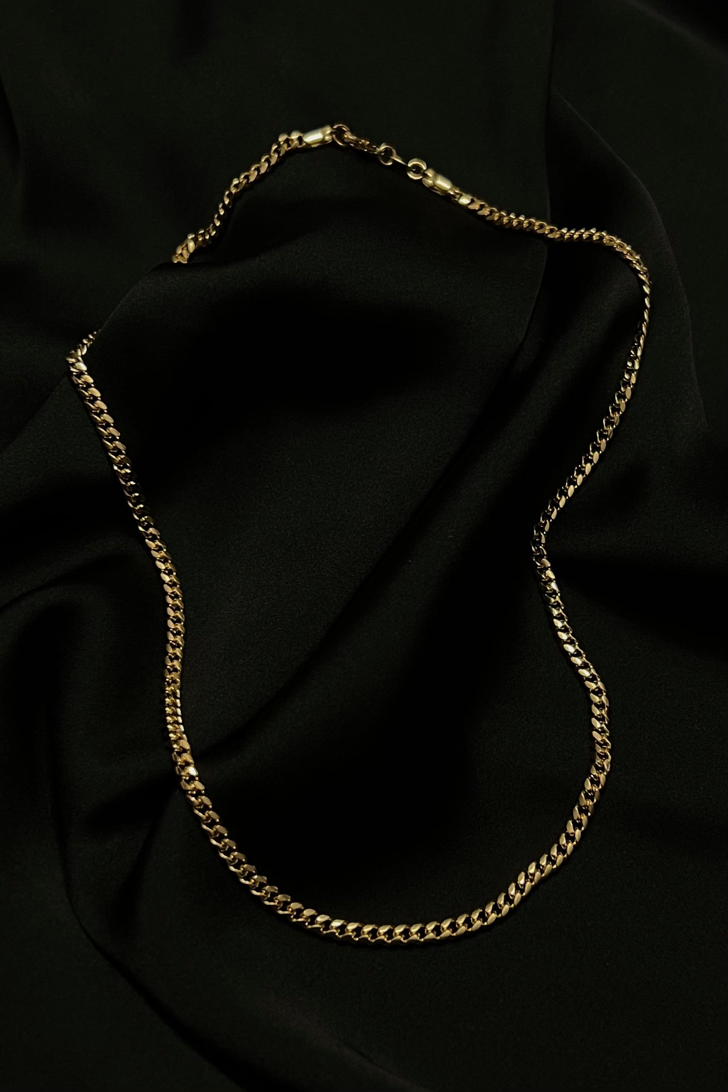 Cuban chain necklace showcased on a luxurious black fabric background. The necklace features interlocking, tightly-woven links.
