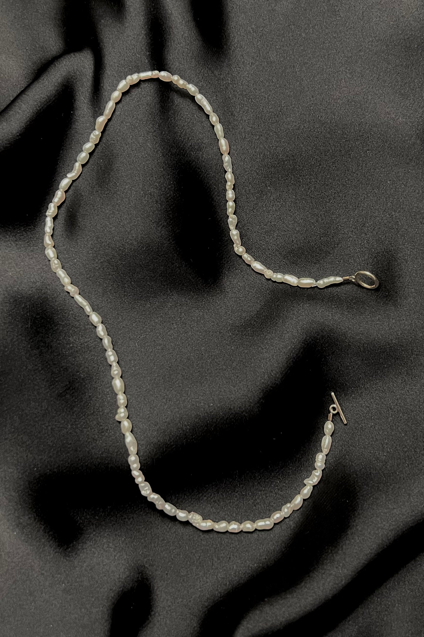 Rice pearl necklace photographed on a shiny black satin fabric.