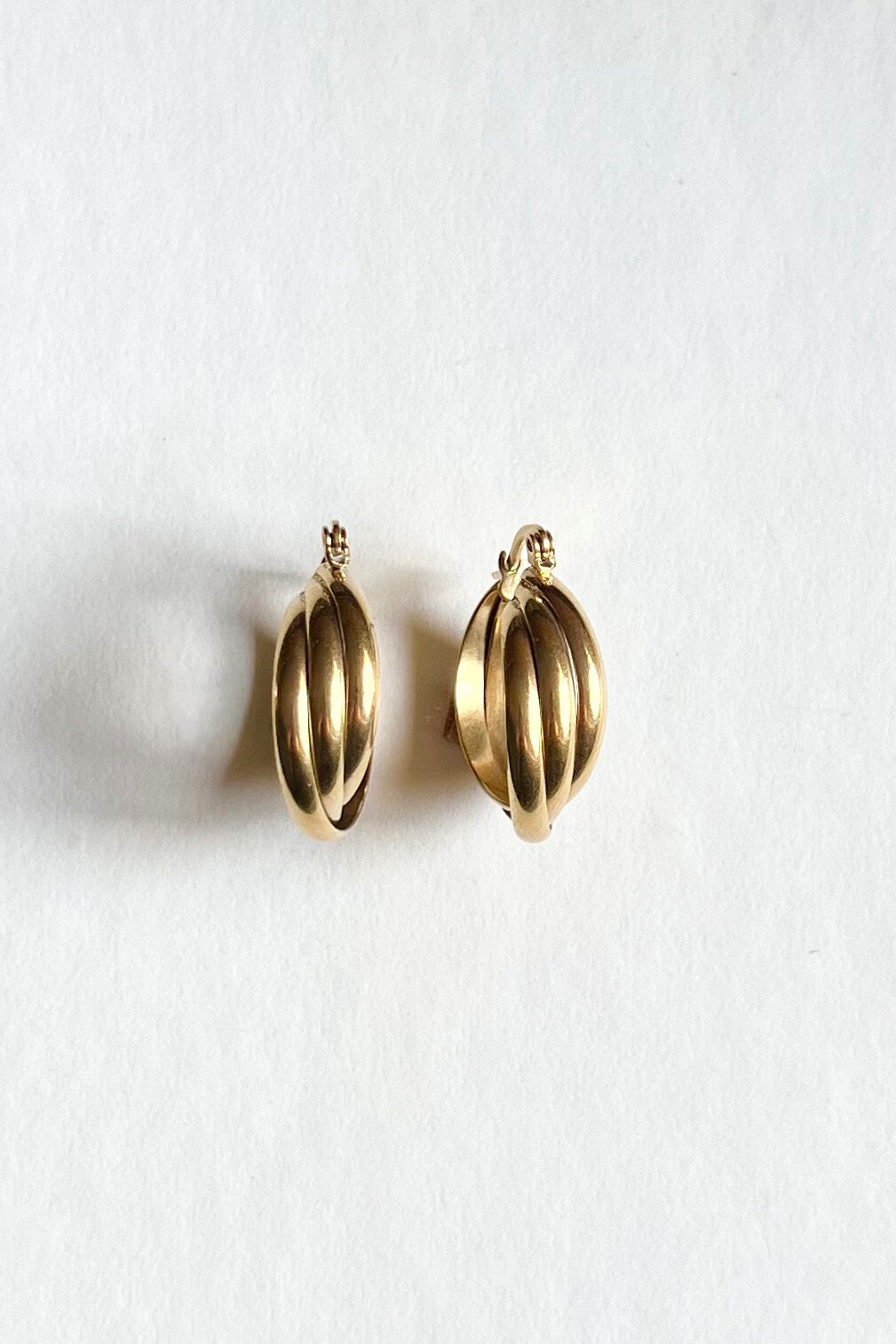 A side view of the gold earrings with three strands of small hoops creatively twisted together, showcased on a clean white background.