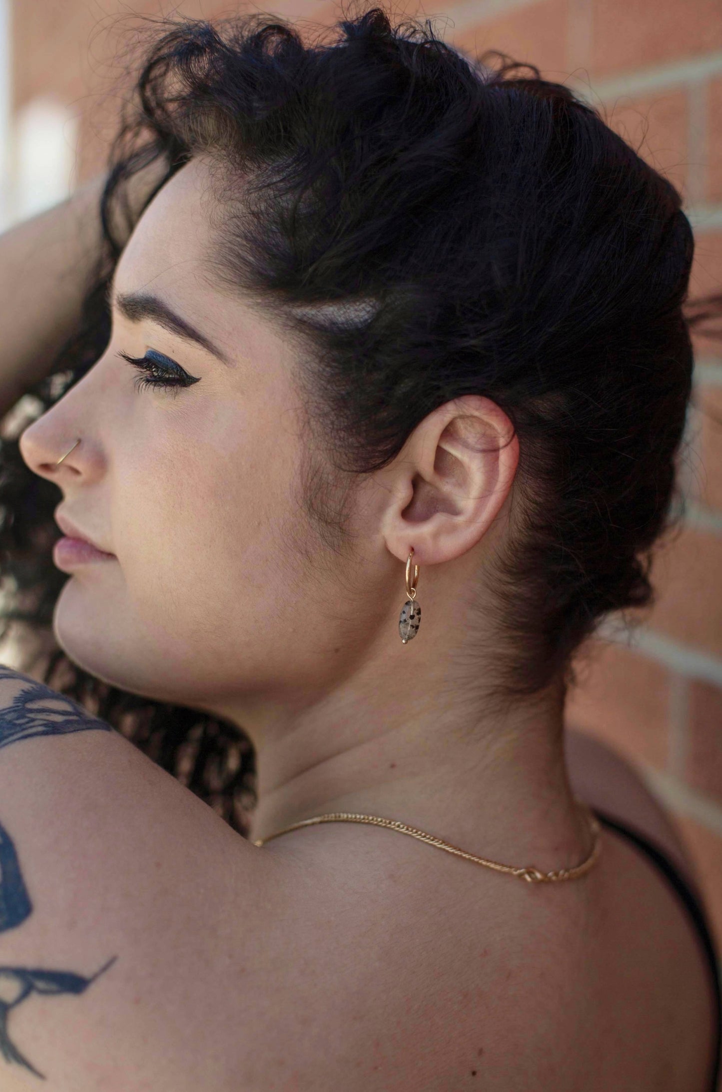 A model showcasing the hoop earrings with Dalmatian-like Black Rutilated Quartz Pendants, beautifully accentuating her look as she lifts her hair to reveal the accessory.