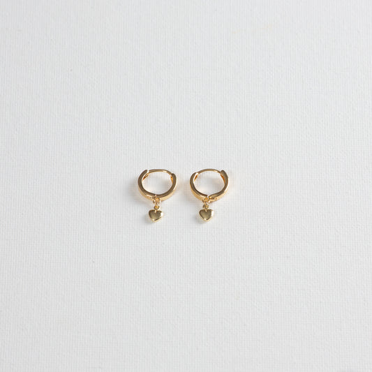 Gold hoops with a small heart charm dangles on each hoop, photographed on a white background.