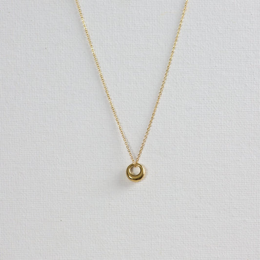 Gold Circle Pendant Necklace on a white background. The pendant features a unique shape, thinner on top and gradually thickening towards the bottom.