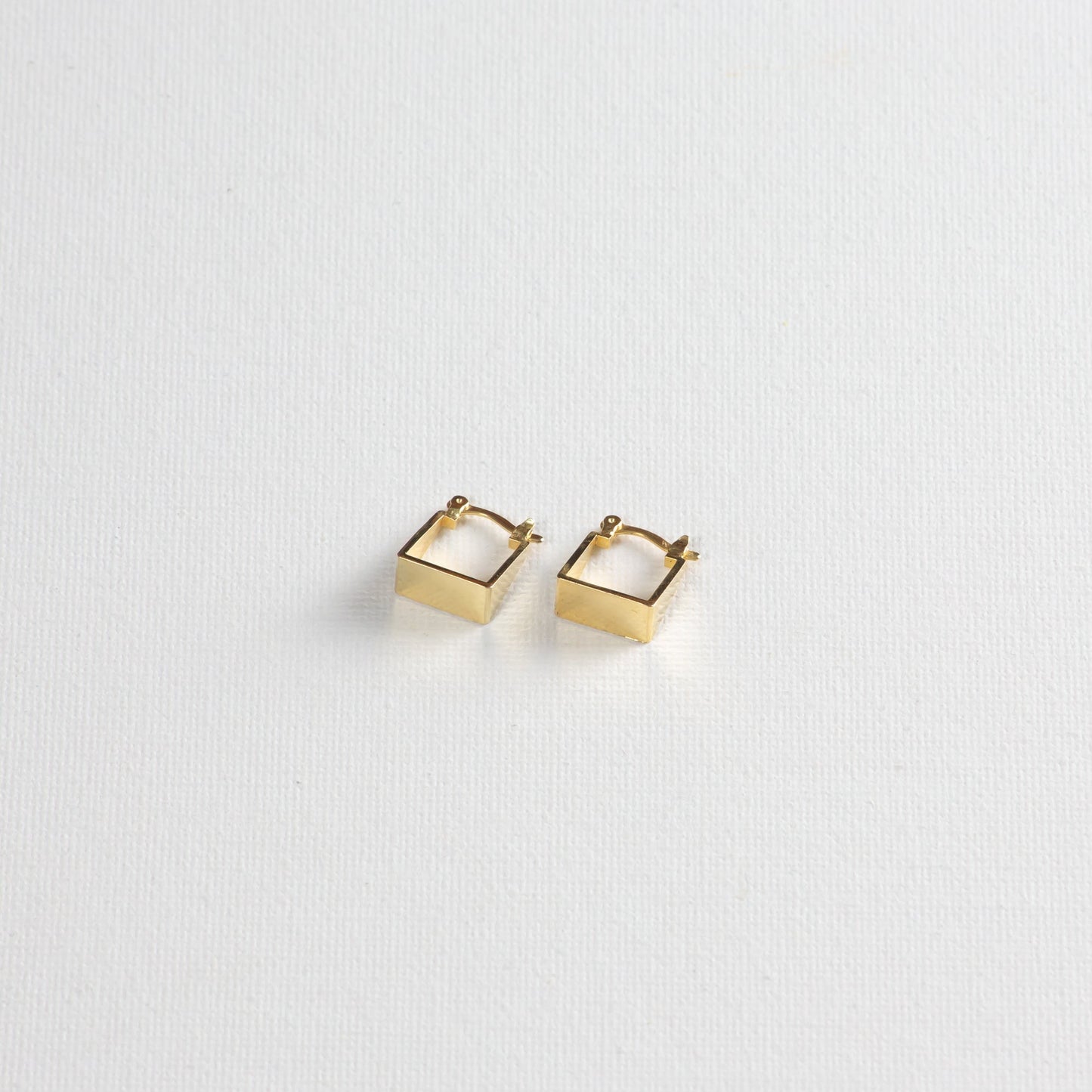 The gold square hoops are photographed at a slight angle from the bottom on a white background. The earrings are carefully positioned, showcasing the corners and edges of the design.