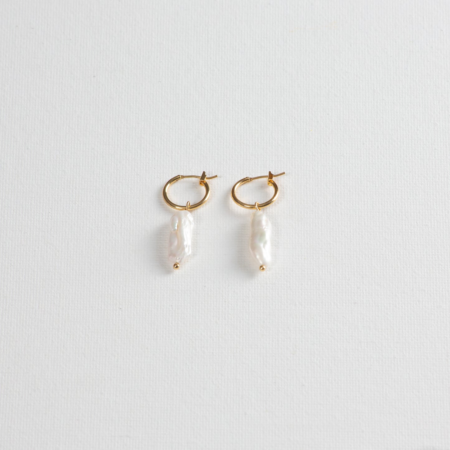 Delicate gold hoops with baroque pearl pendant on a white background.