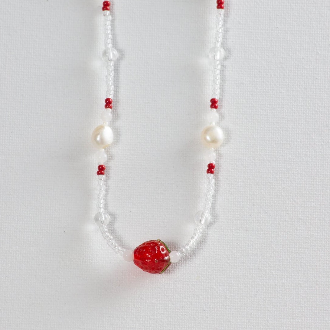 Beaded necklace with primarily small clear glass beads and accents of larger clear glass beads, pearl, red, milky white beads to add texture and pops of color. The necklace is photographed on a white background. 