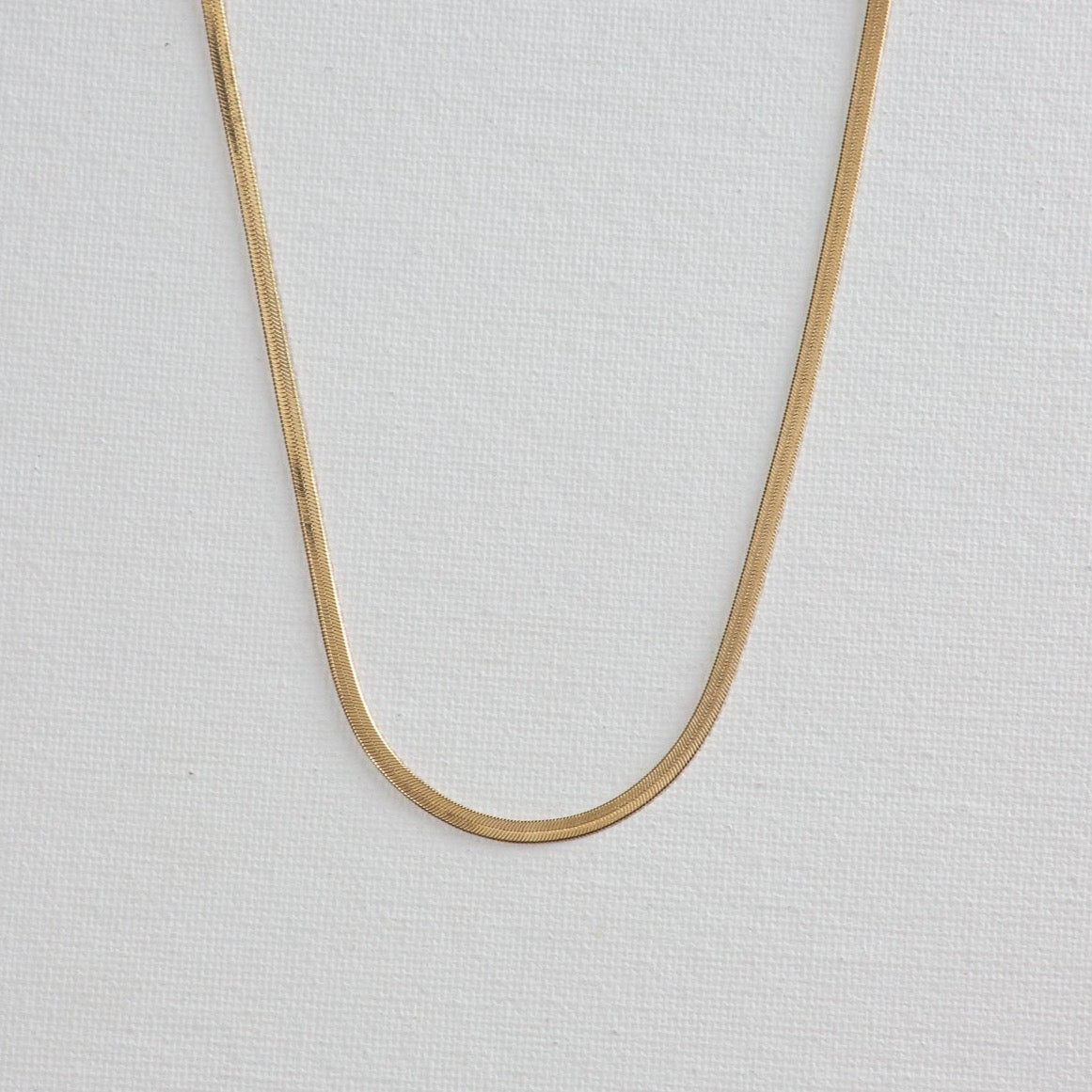The gold necklace laying flat on a white background.