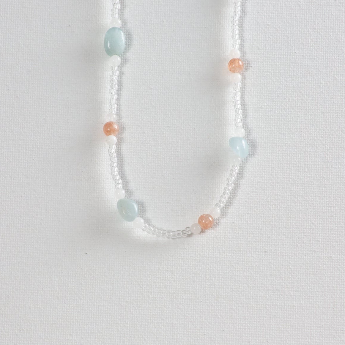 Predominantly clear beads with accents of soft pink and pastel blue glass beads on a white background.