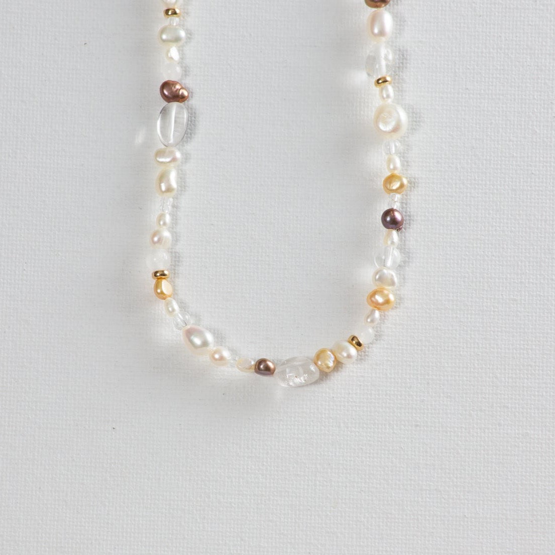Nova necklace on a white background. In the photo, you can see the combination of peach, cream, and purple colored pearls alternating between clear glass beads and dainty gold beads.
