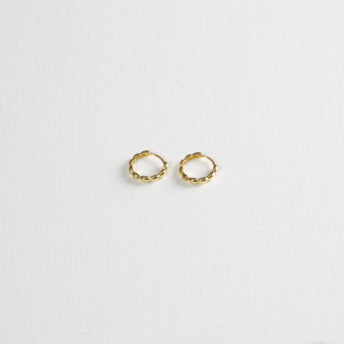 Oryza hoops, gold hoops with rounded textures, photographed on a white background. The photo is taken at a slight angle from the bottom.