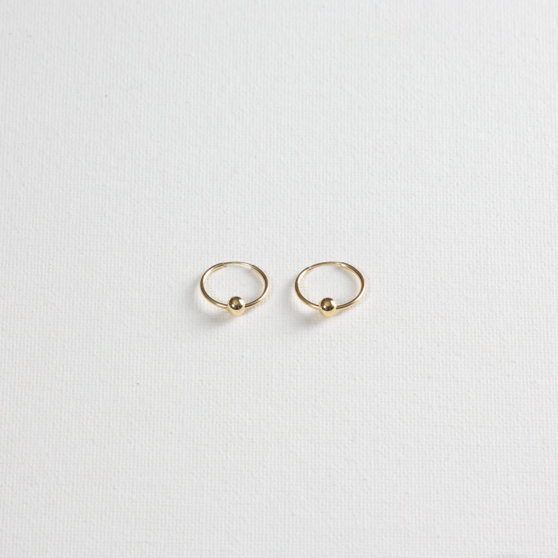 Thin gold hoops with seamless closure. The earrings feature delicate 4mm circle looped through the earring. The earrings are photographed on a white background.