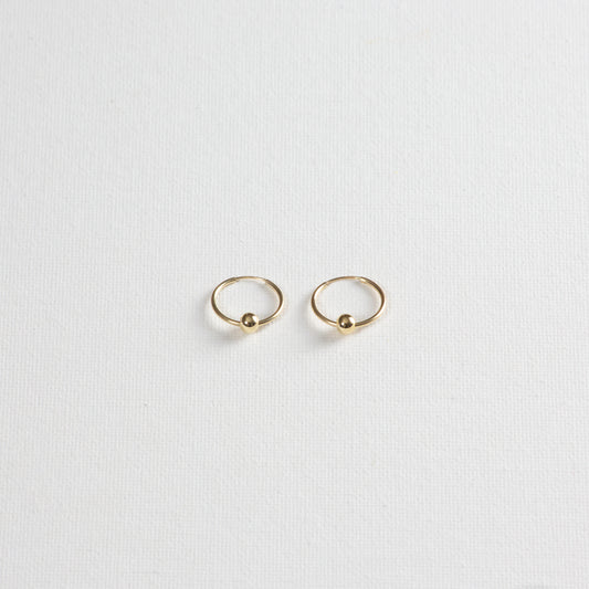 Thin gold hoops with seamless closure. The earrings feature delicate 4mm circle looped through the earring. The earrings are photographed on a white background.
