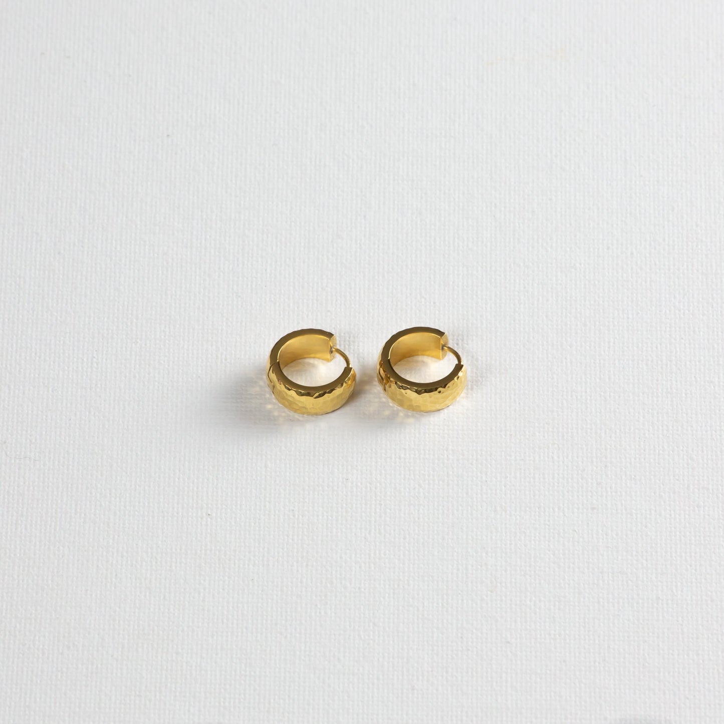 The earrings photographed on a white background on a slight angle from the bottom. It subtly shows the hammered texture on the side.