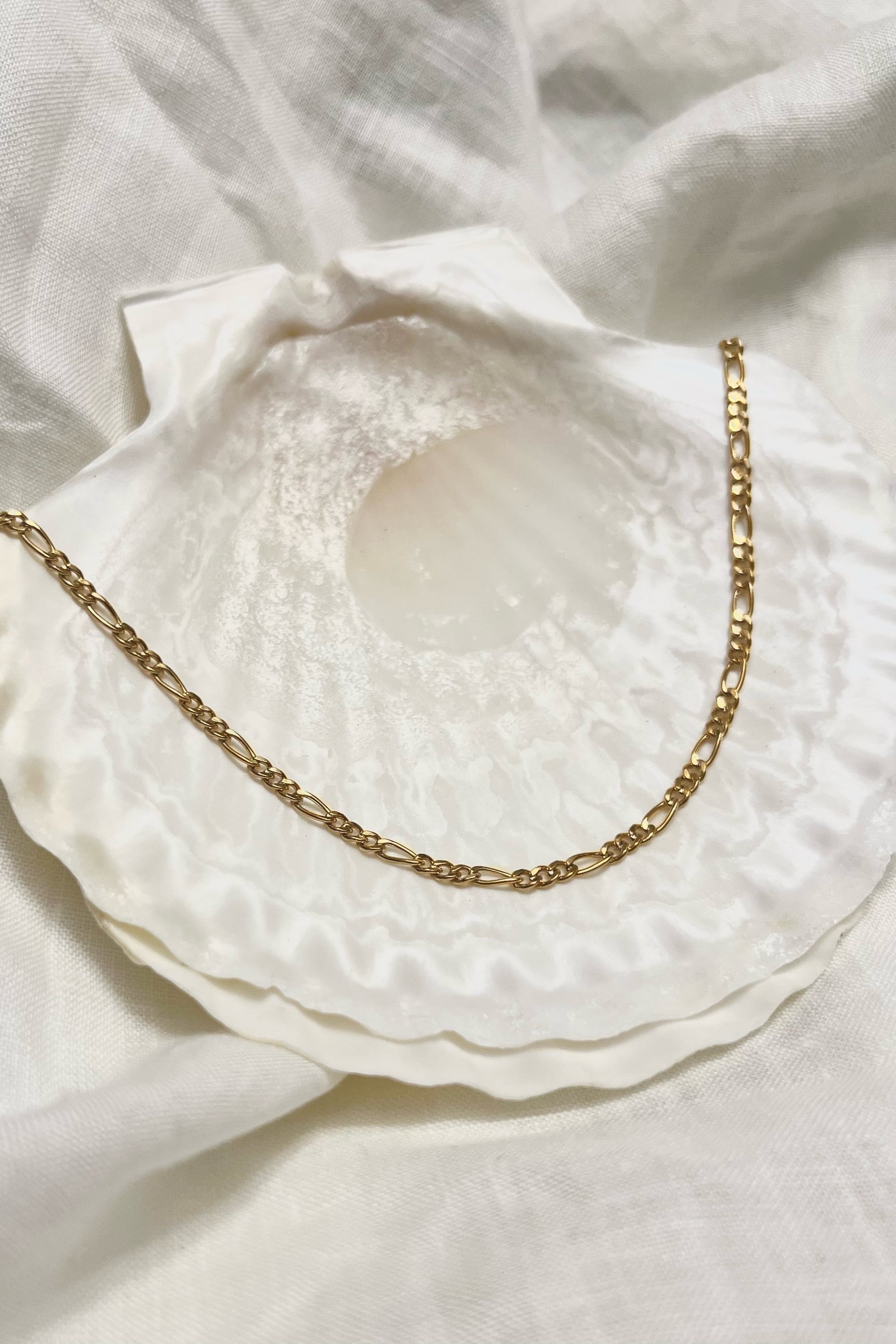 A styled photo of the necklace on top of a white shell and white linen background.