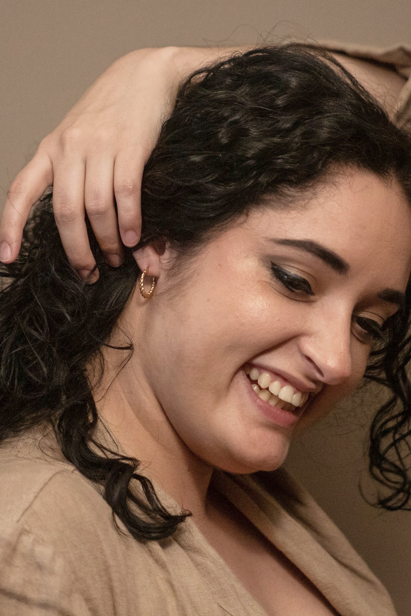 A photo showcasing the happy face of the model, while she pulls her hair back to show the earring.