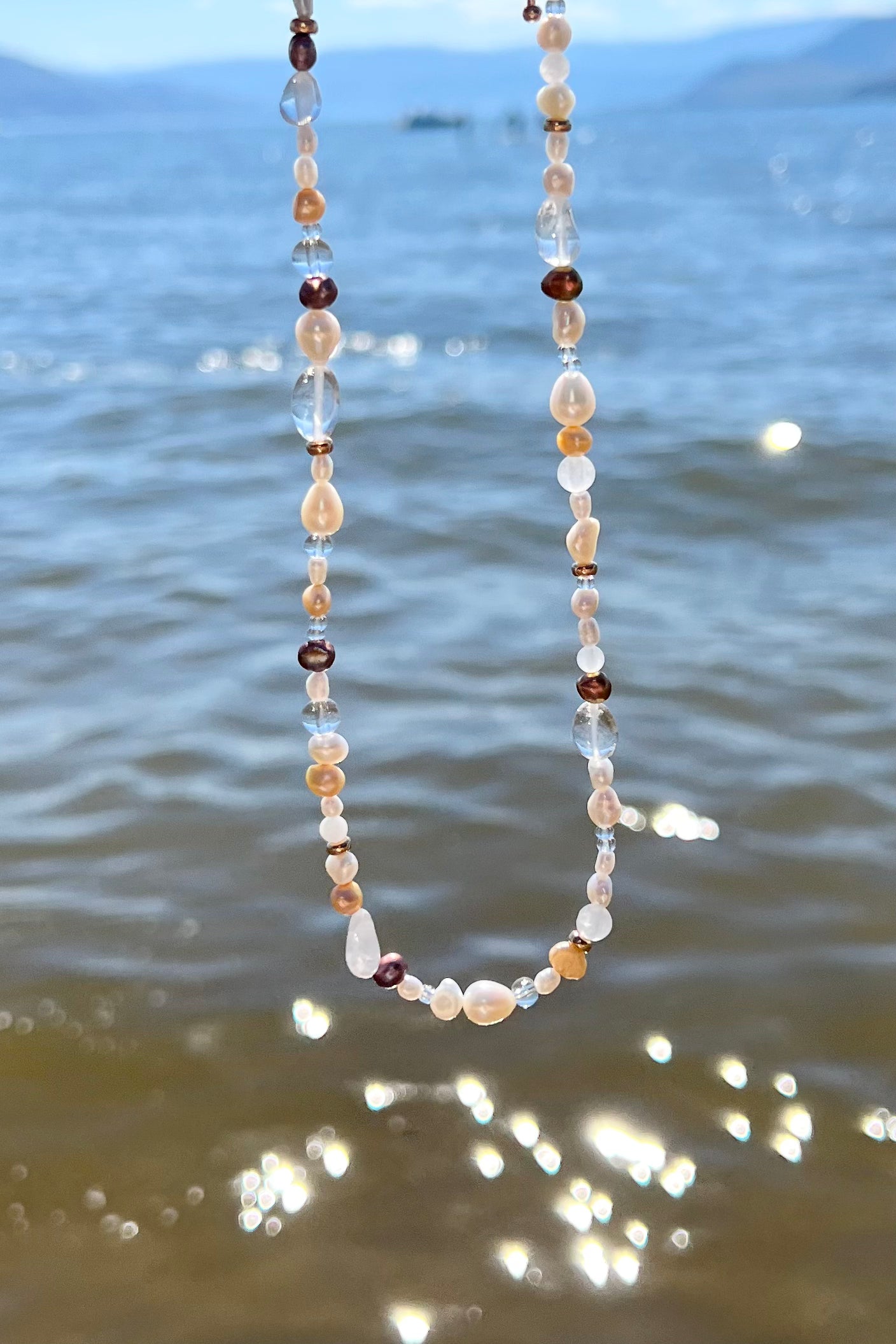 Nova necklace photographed at the beach, with the beach water background, showcasing how the necklace looks like in bright, direct sunlight.