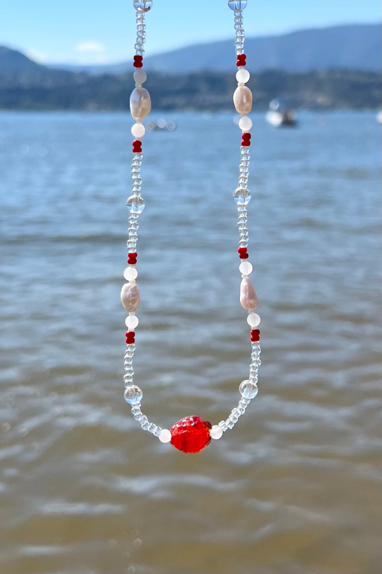 The strawberry necklace in bright, direct sunlight at a beach setting.