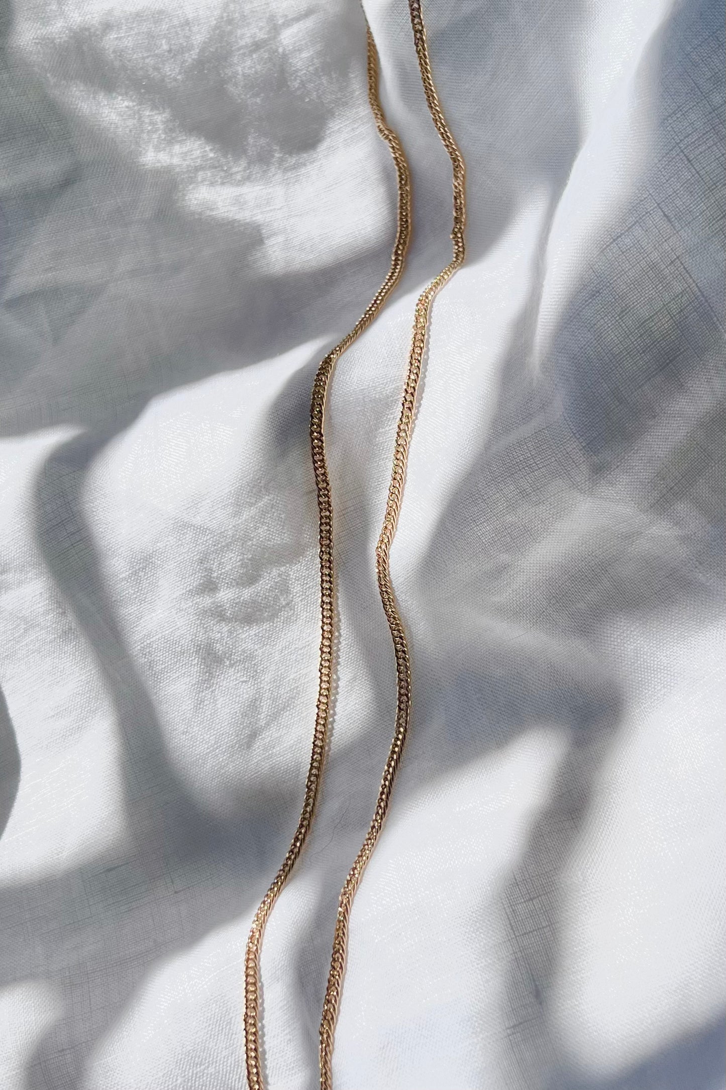 Gold Curb Chain Necklace beautifully draped on a linen surface, elegantly following the curves of the linen folds.