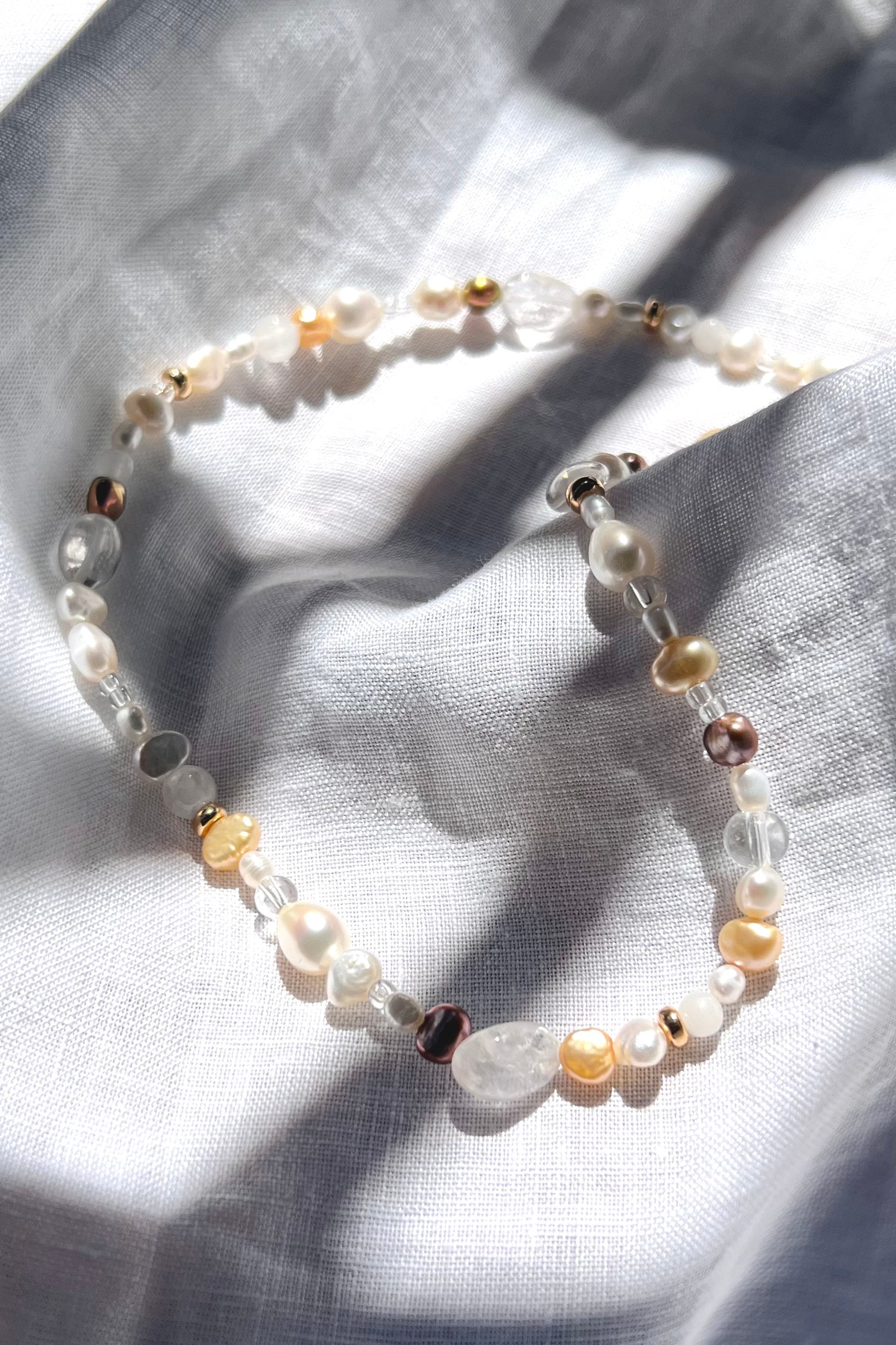Nova bead necklace placed on top of a white linen. The necklace follows the curves and flow of the linen, showcasing subtle sparkle from the beads.