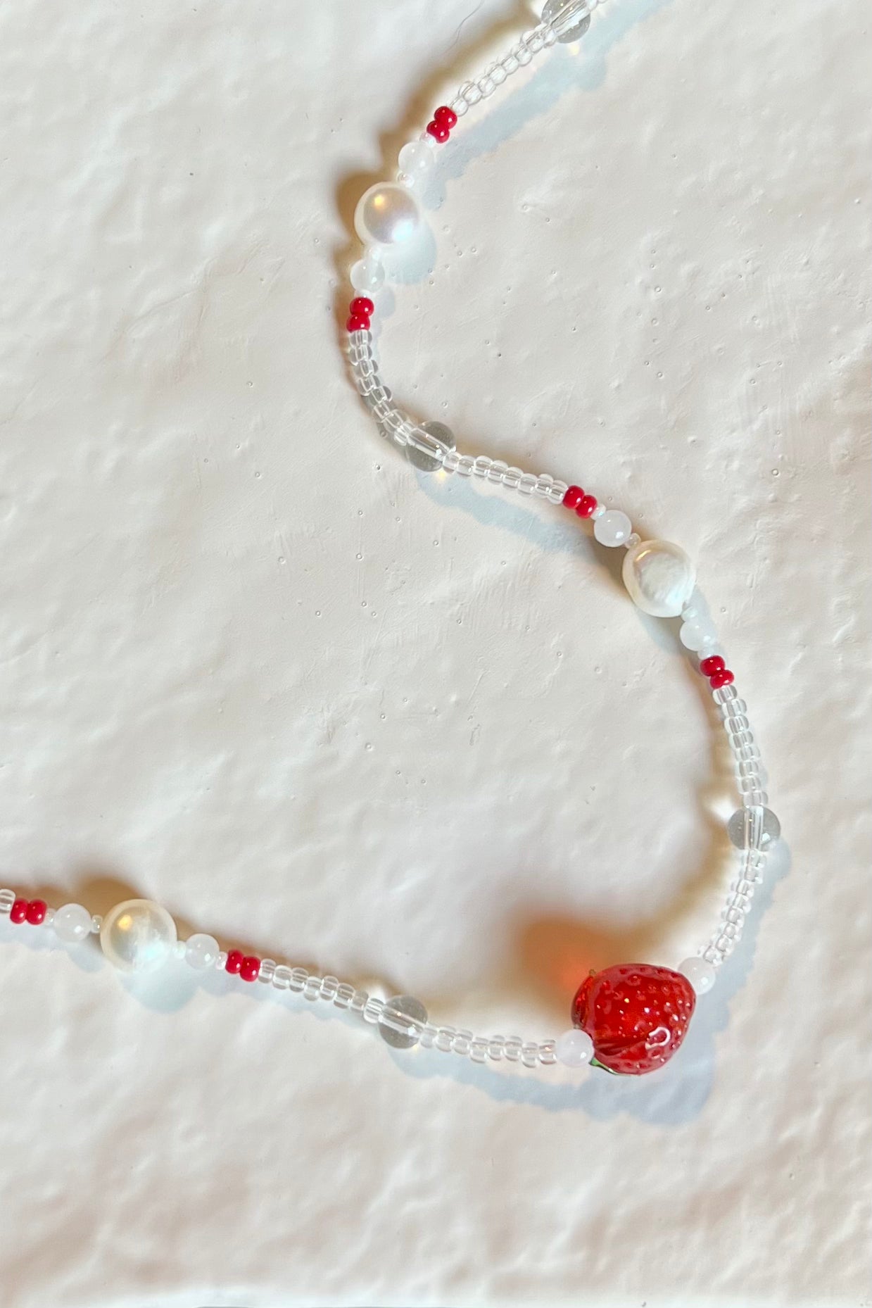 A closeup photo of the strawberry necklace placed on top of a texture white ceramic plate.