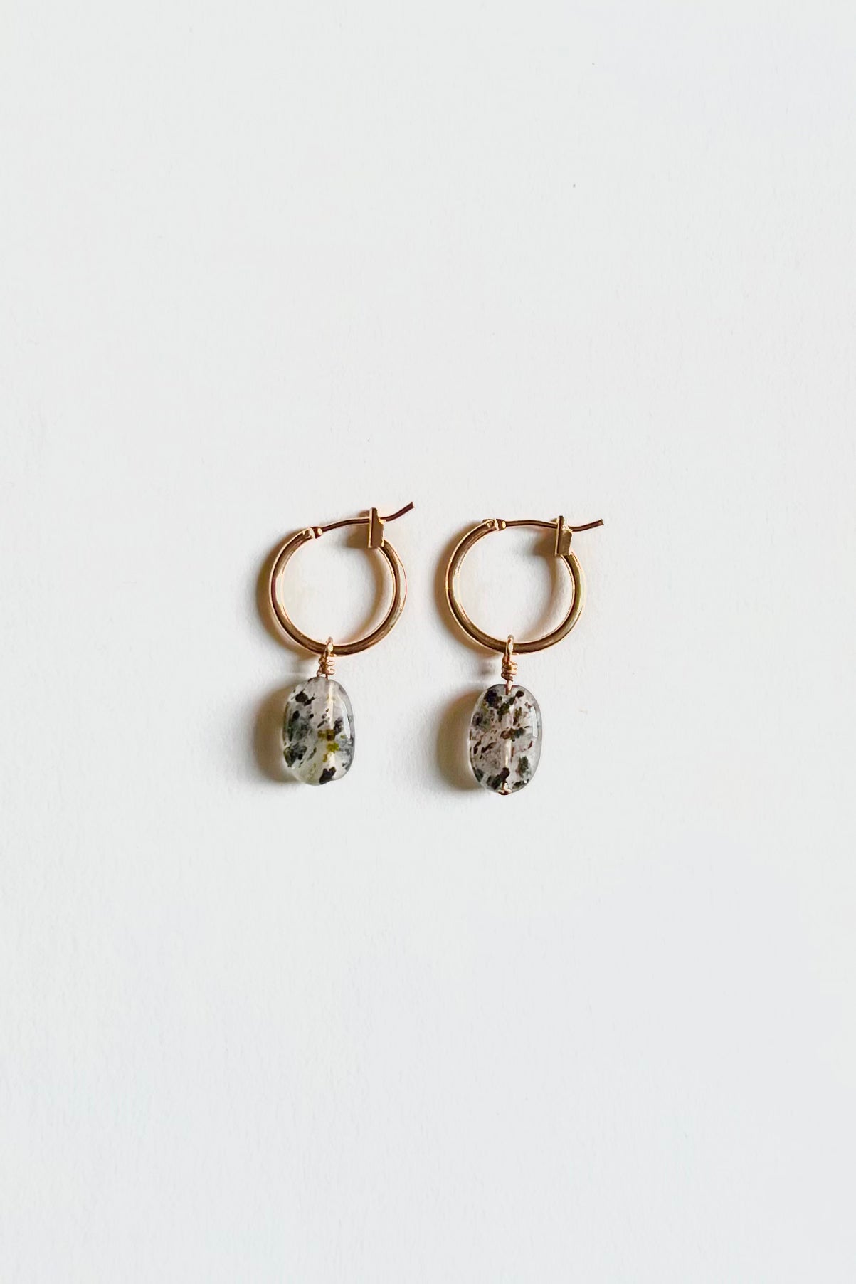 Gold hoop earrings with Dalmatian-like Black Rutilated Quartz Pendants, showcased on a clean white background with top view angle.