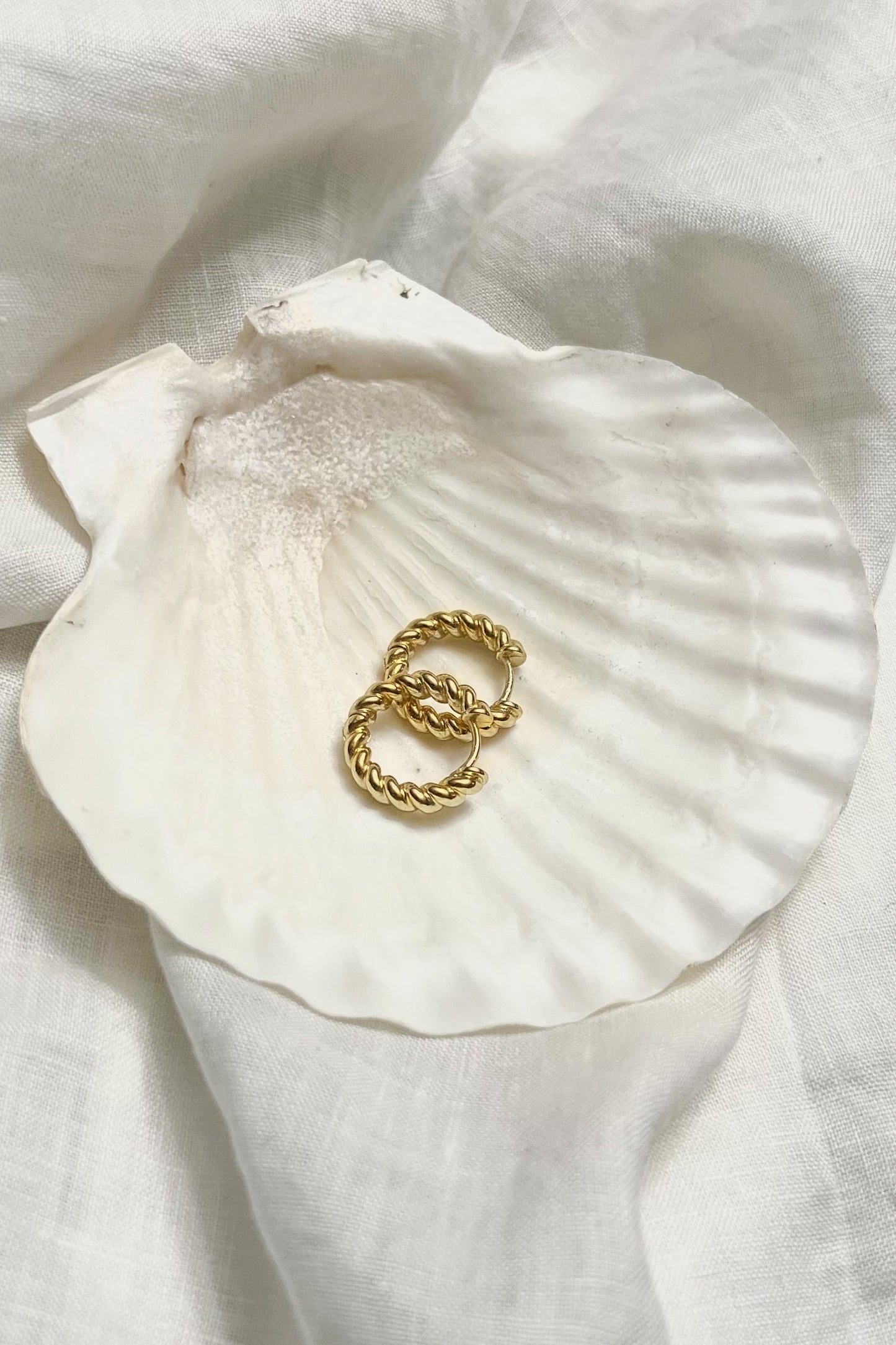 Styled photograph of the Honey crueller hoops from top view angle, placed on a white shell with flowy white linen background.