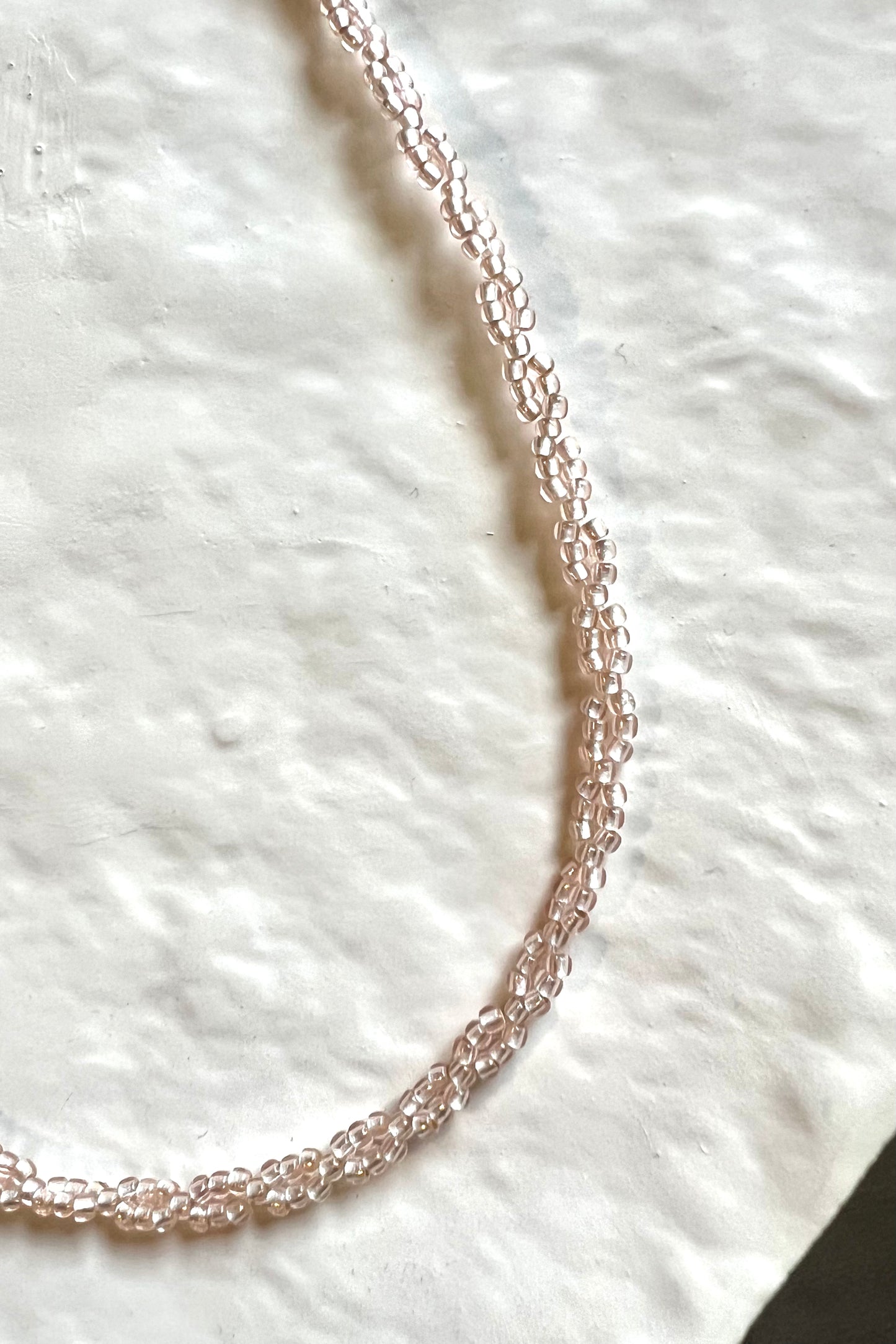 A zoomed in photo of the choker, highlighting the color and patter of the beads. The choker is placed on a textured, white clay plate.